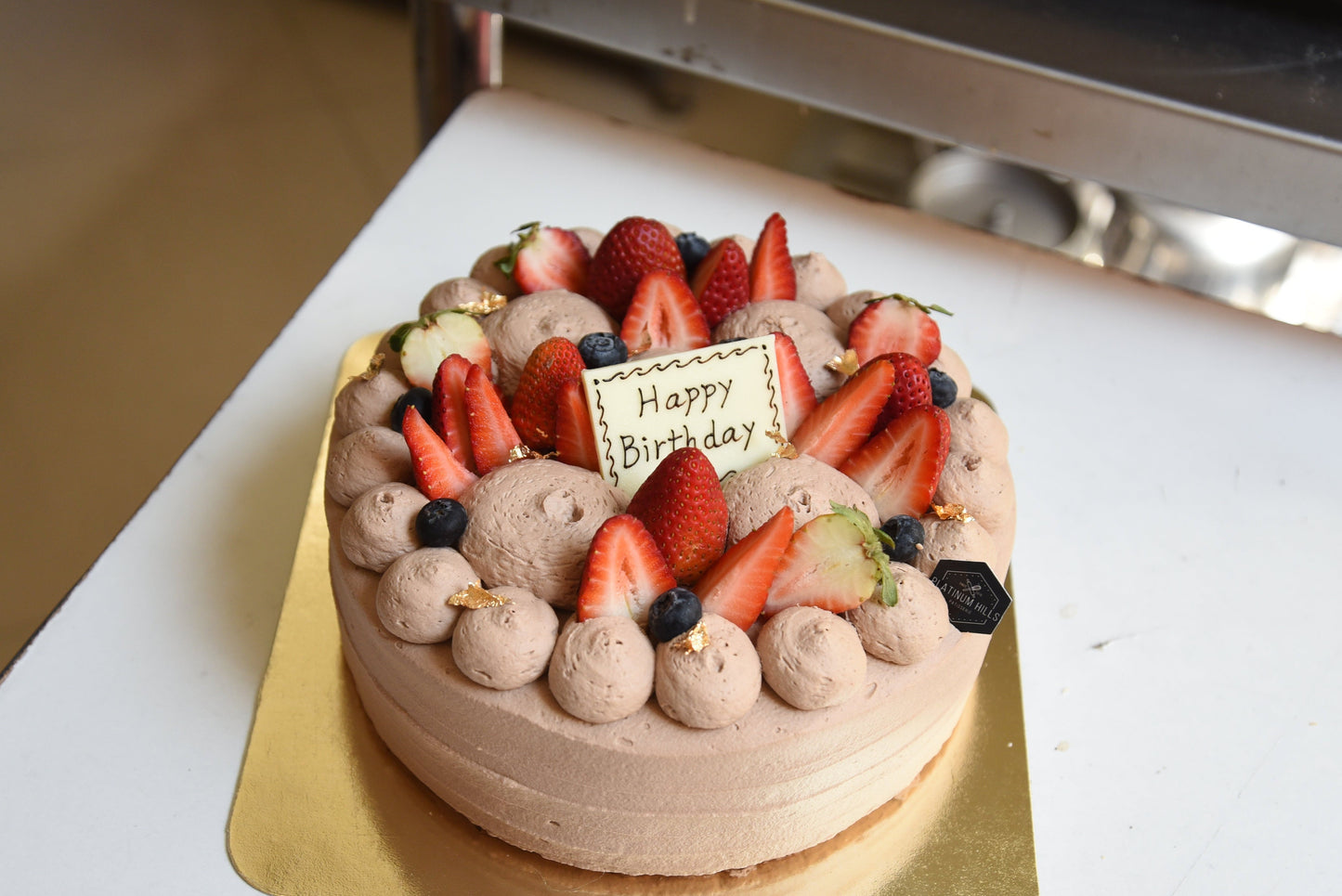 Chocolate shortcake with strawberries and a 'Happy Birthday' card on a white surface.