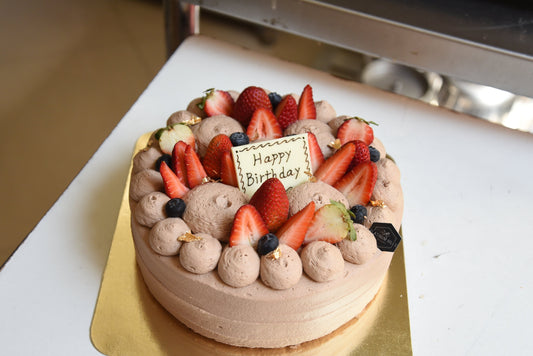 Chocolate shortcake with strawberries and a 'Happy Birthday' card on a white surface.